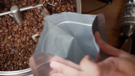 person pouring spoonfuls of roasted coffee beans into a bag for export