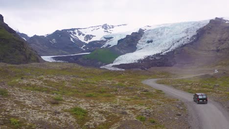 Antenne-über-Einem-Schwarzen-Wohnmobil,-Das-Zu-Einem-Abgelegenen-Gletscher-In-Den-Bergen-Islands-Fährt-1