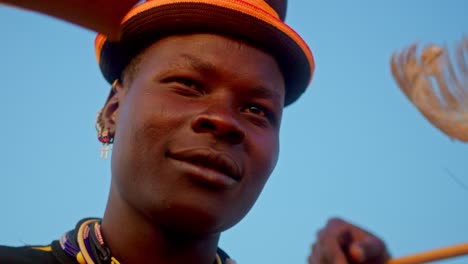 a traditional african man wearing a feathered hat smiles at the camera in karamoja, uganda, africa - close up