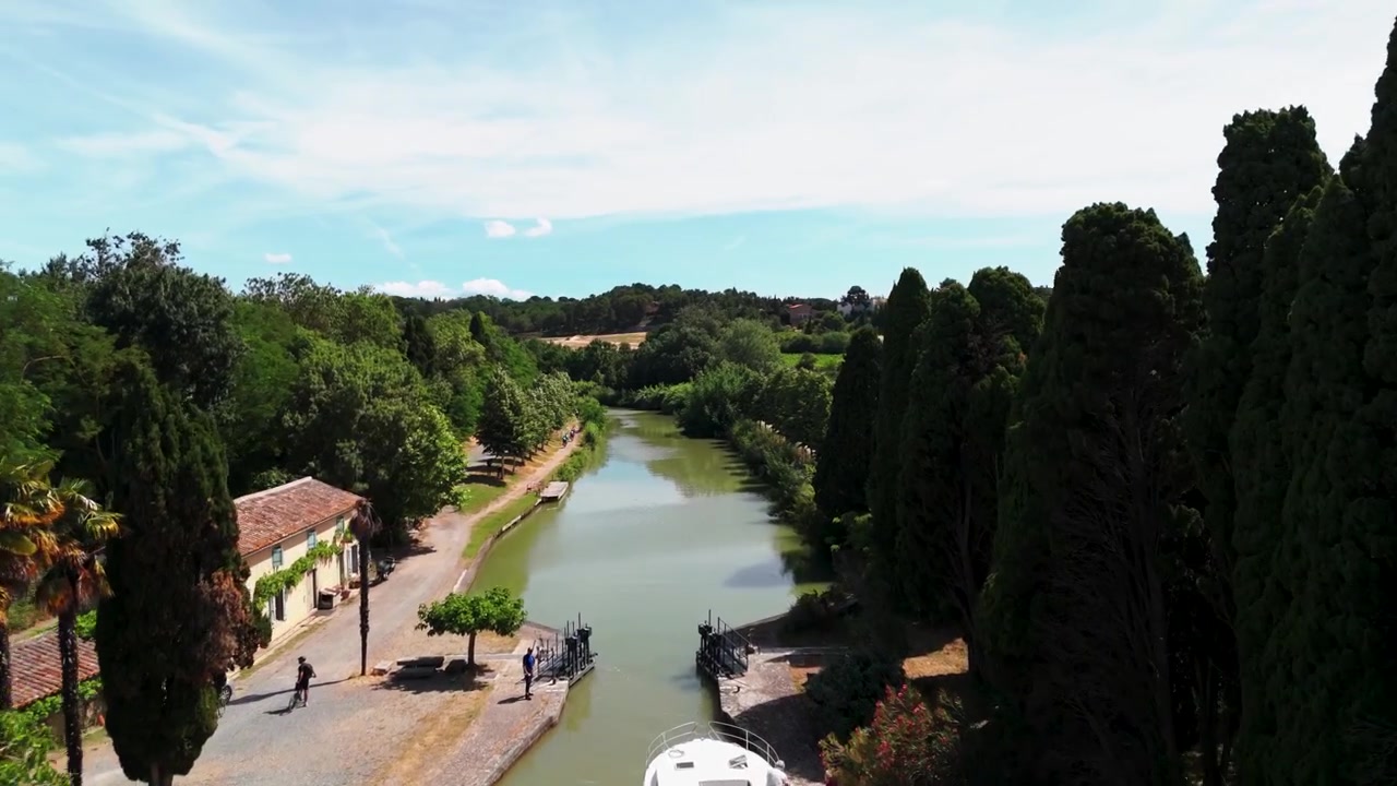 Una barca attraversa una chiusa di canale circondata da una vegetazione lussureggiante e sentieri rurali