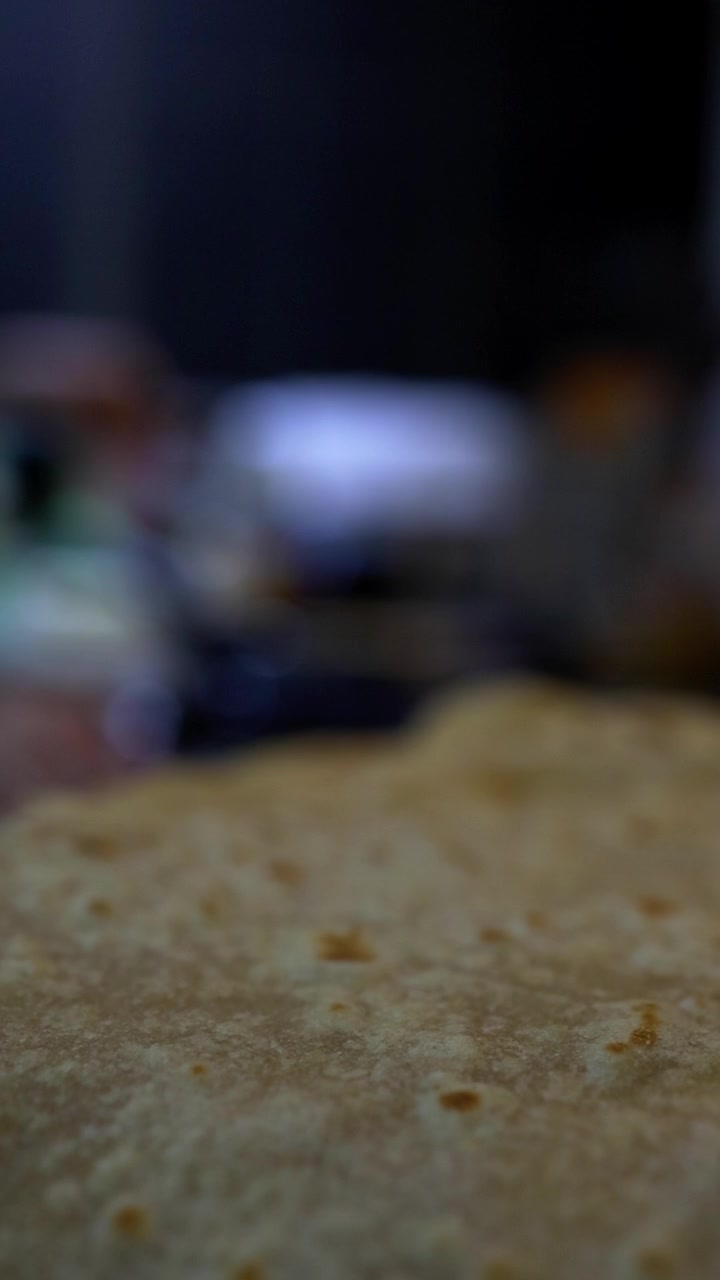 Extreme close-up of freshly cooked chapati flatbread with visible brown spots and texture, shallow depth of field with blurred kitchen setting and blue cookware in background. Warm, intimate cooking s