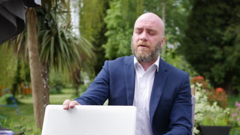 a tired business man working on a laptop at home in his garden