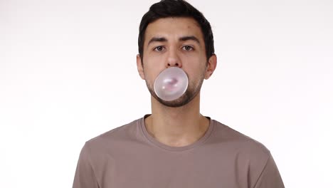 vista frontal de un europeo de cabello oscuro, un joven de cerdas soplando una burbuja de chicle con los ojos bien abiertos aislado sobre un fondo blanco. chicle estalla. cámara lenta