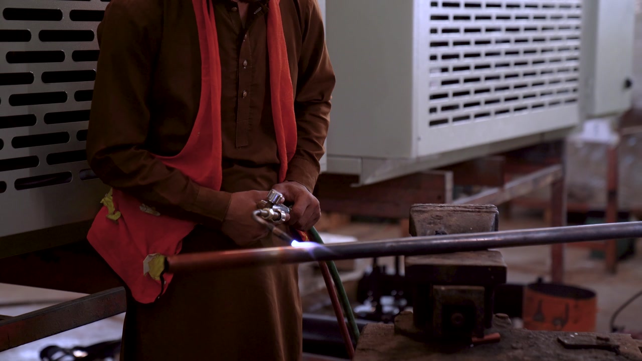 Metal Worker Using A Torch To Heat Up Copper Pipe In A Metalworking Fabrication Plant In Pakistan.