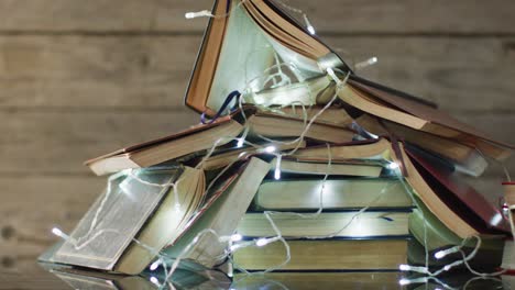 video of christmas fairy lights and stack of books on wooden background