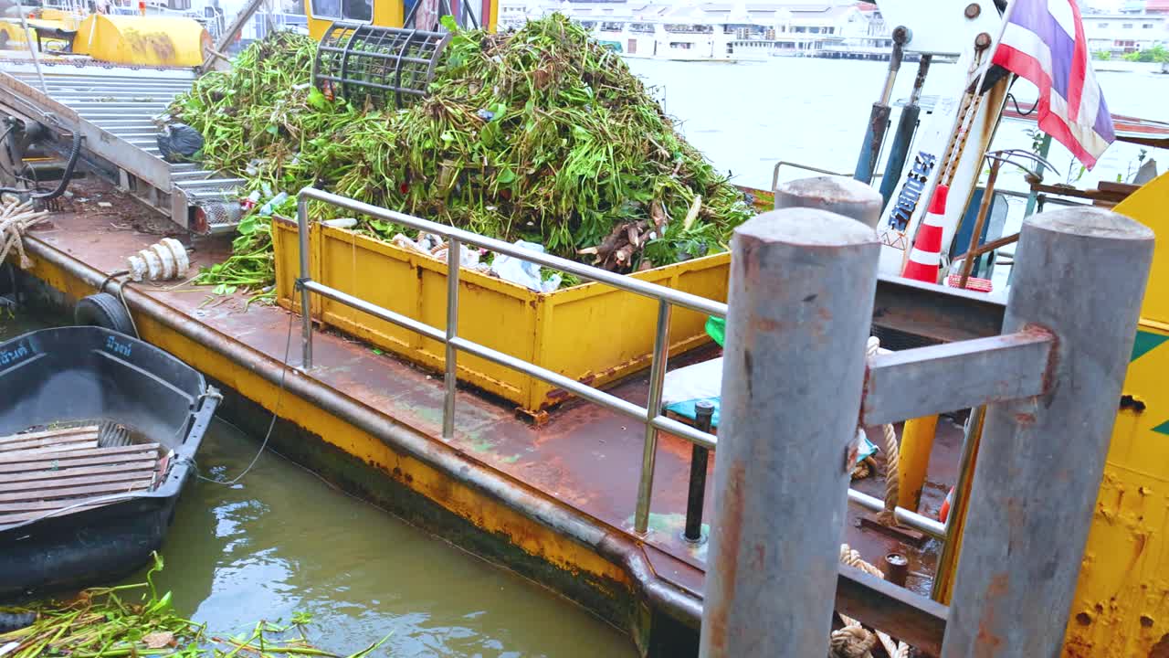 A garbage boat collects river debris in Bangkok, Thailand. Bright daylight, industrial setting, and efficient waste management captured