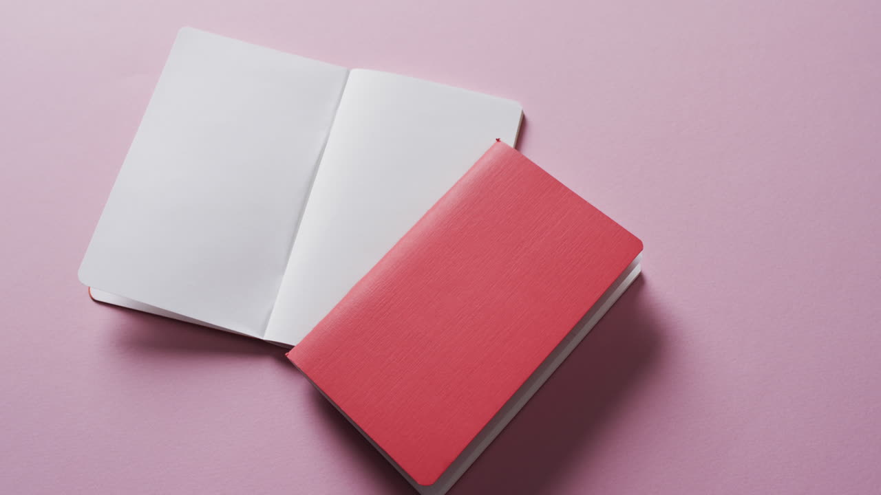 Close up of open blank book and red closed book with copy space on pink background in slow motion