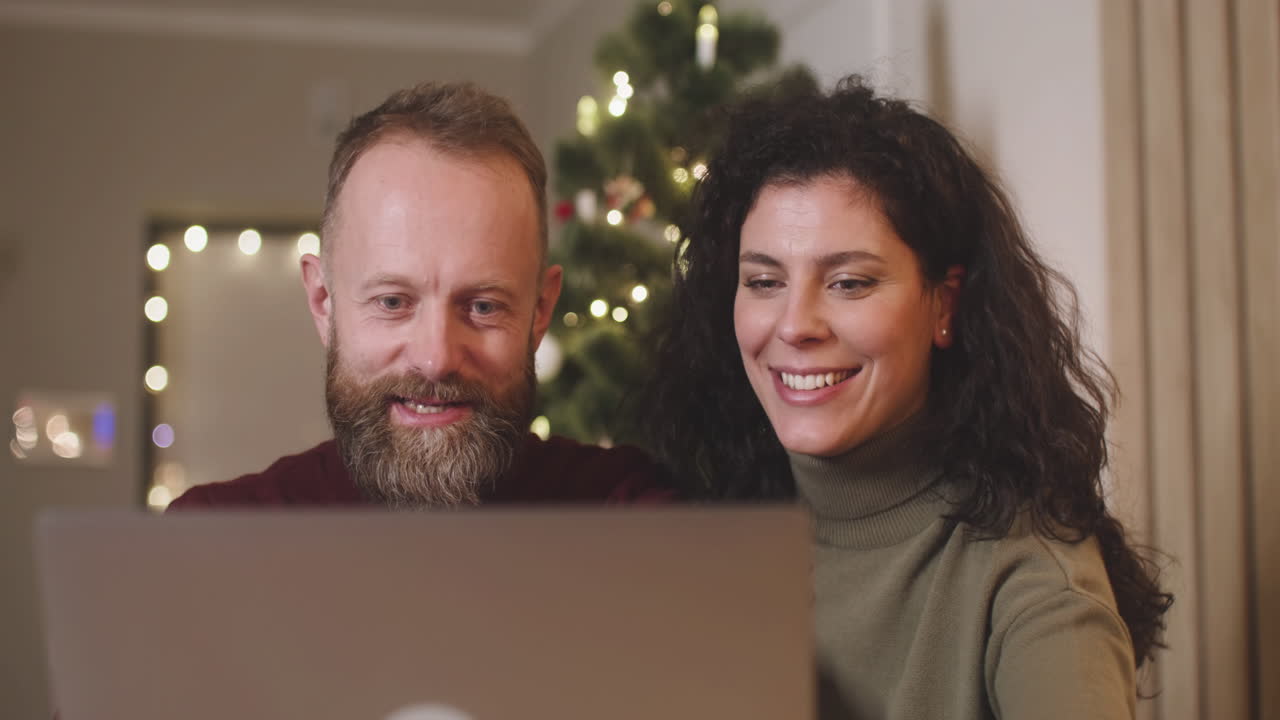vista frontal de una pareja usando una computadora portátil en una habitación decorada con un árbol de navidad 1