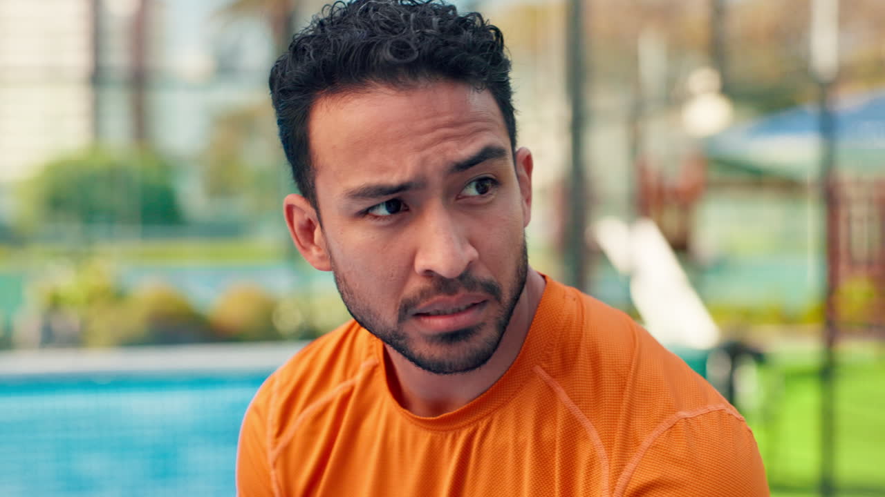 Focused Young Man in Orange Shirt Observing Something Outdoors