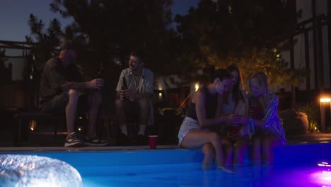 two guys and three girls chat, drink drinks and relax near the pool during their vacation in a country house in the evening