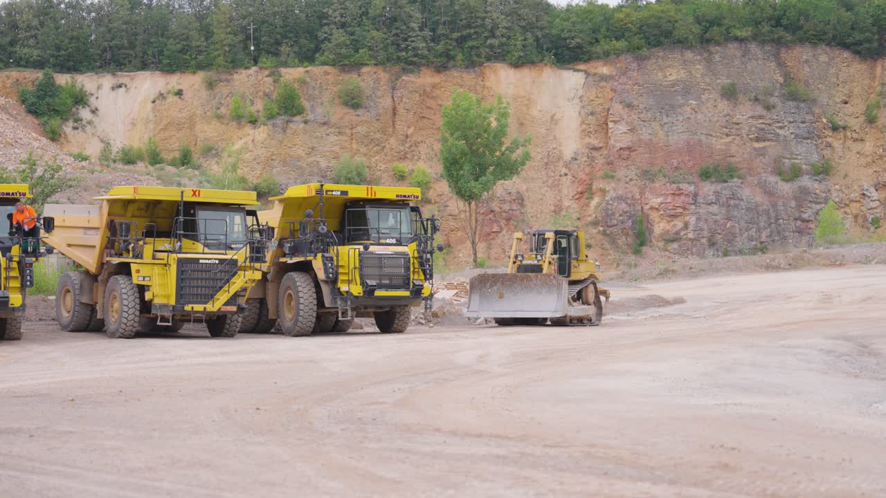 Bulldozer vehicle drive near big trucks at limestone quarry, Czechia