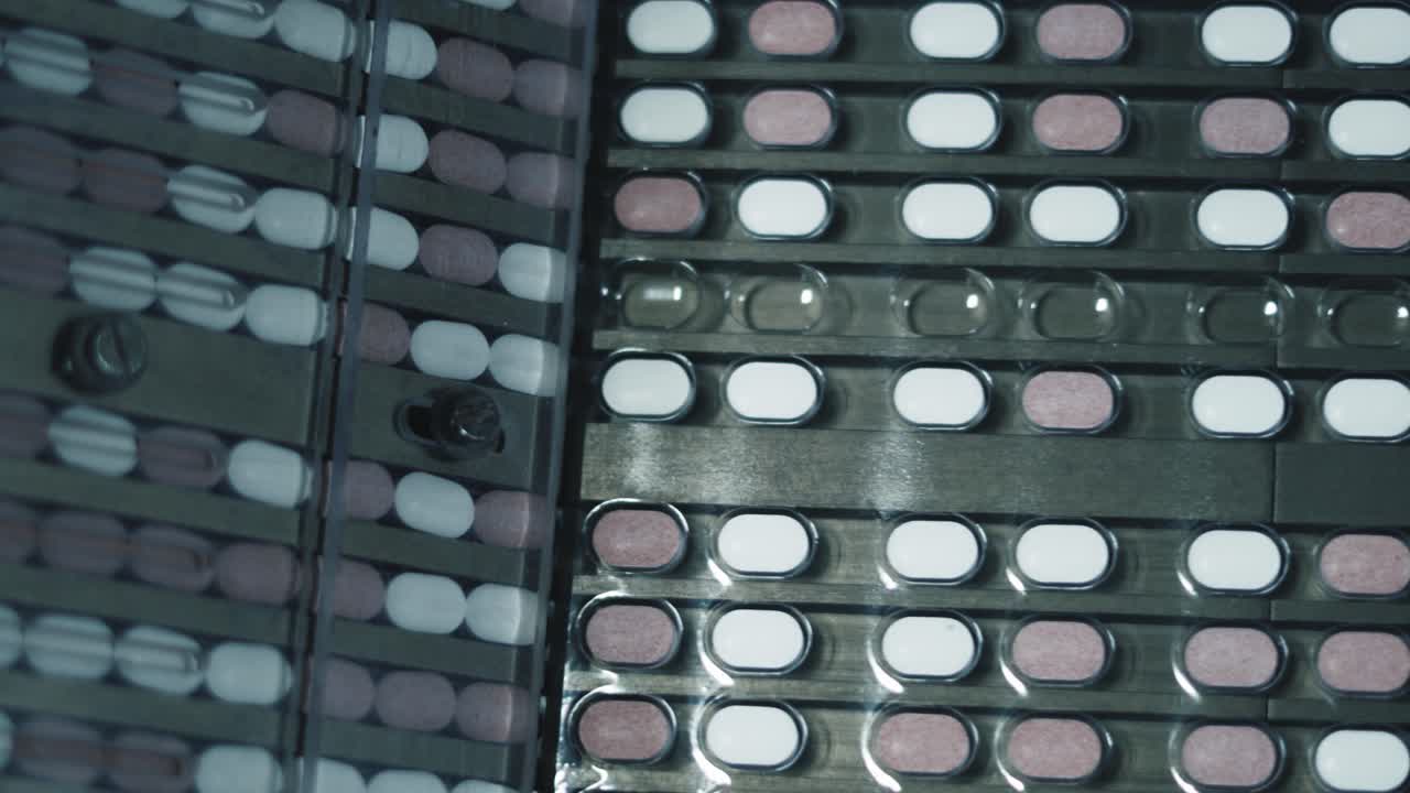 Macchinario che deposita pillole di medicinale negli spazi vuoti delle confezioni, con operai che intervengono per risolvere eventuali guasti.