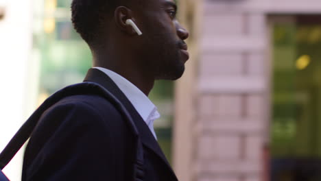 young businessman wearing wireless earbuds streaming music or podcast from mobile phone walking to work in offices in the financial district of the city of london uk 3