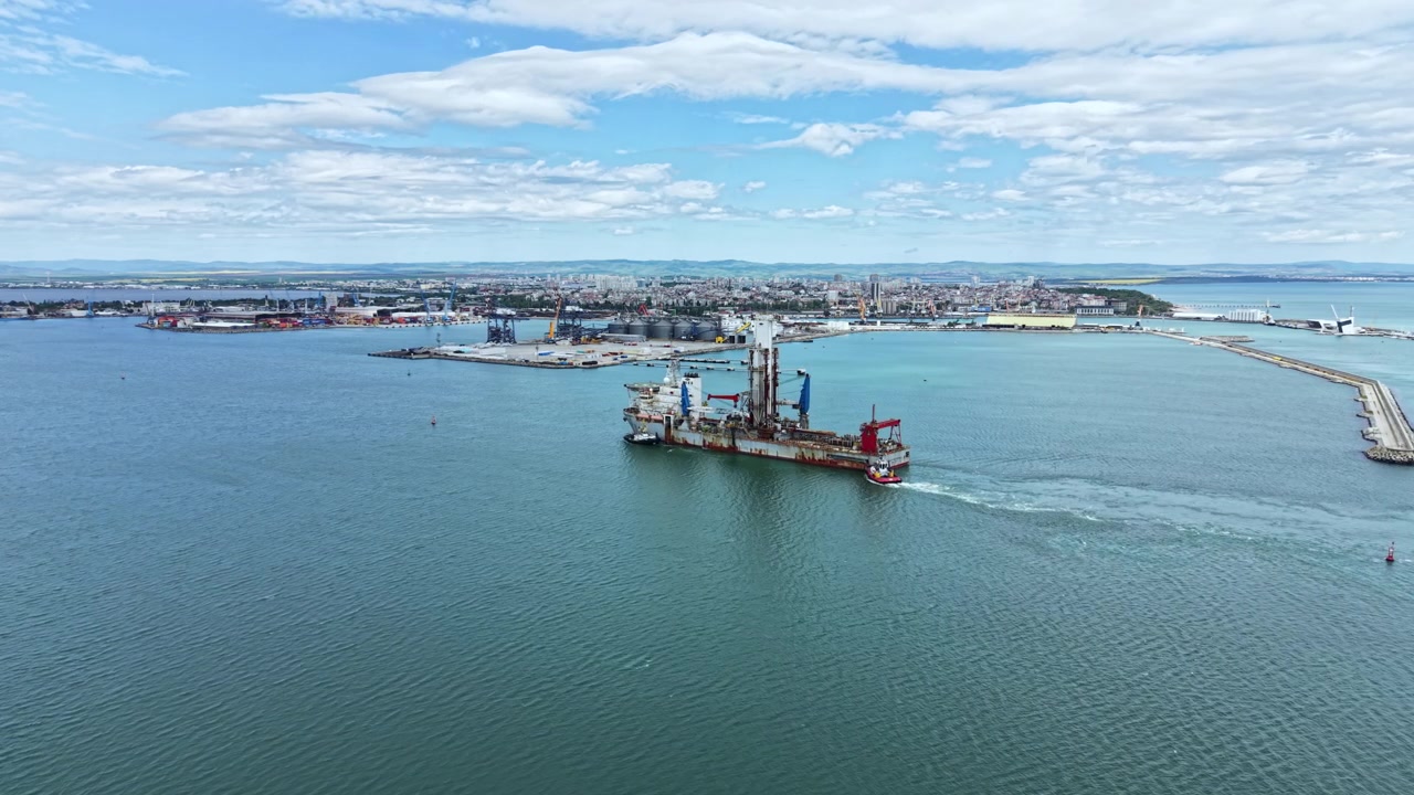 Industrial dredging vessel operating in harbor near coastal city with surrounding infrastructure and water