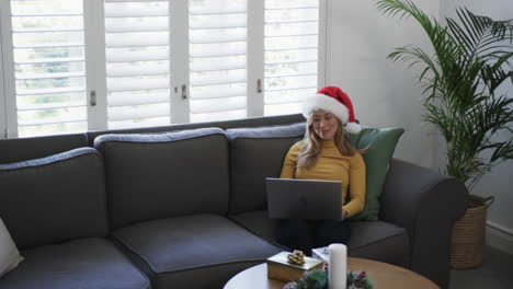 Fröhliche-Biracial-Frau-Mit-Weihnachtsmütze-Und-Laptop-Zu-Weihnachten,-Kopierraum,-Zeitlupe