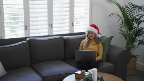 mujer biracial feliz con sombrero de santa usando portátil en navidad, espacio de copia, cámara lenta