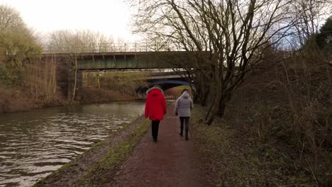 2-women-take-a-walk-along-by-the-former-industrial-canal-in-Stoke-on-Trent,-a-poverty-stricken-area-featuring-many-factories-in-ruins-along-by-the-canal