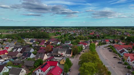 Drone-shot-of-a-small-village-in-Lithuania-surrounded-by-green-fields-under-the-clear-sky,-Sveksna