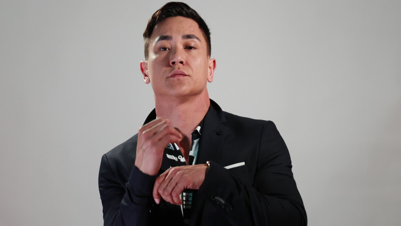 슬로모션의 매력적인 아시아 모델은 재킷이 있는 흰색 배경 앞에 있는 웹 사이트 또는 소셜 미디어를 위한 전자 상거래 사진 촬영 중에 포즈를 바꾸고 포즈를 변경합니다.