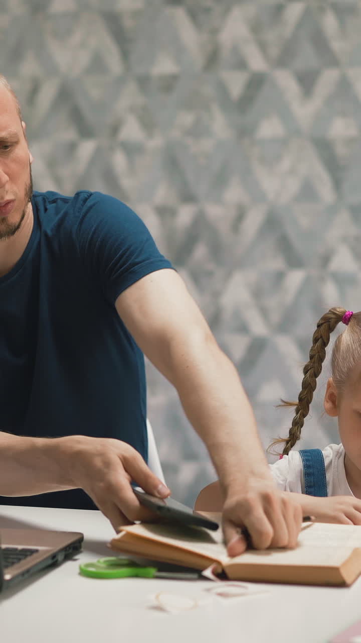 closeup of young daddy sitting at computer in room of house, gives little daughter student with long hair book and pencil to perform homework, recorded at school
