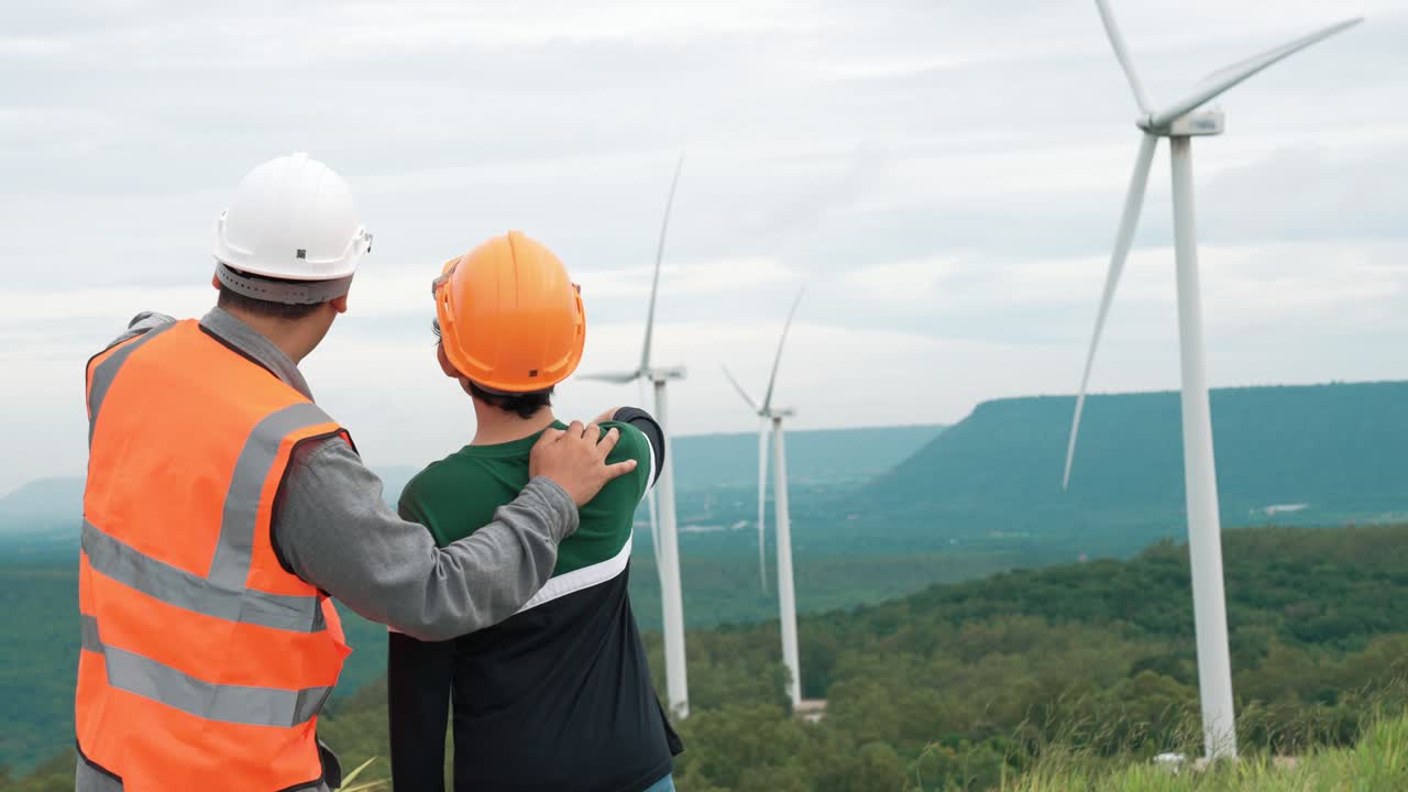 발전적인 엔지니어와 그의 아들이 산 꼭대기의 풍력 발전소에 있습니다.