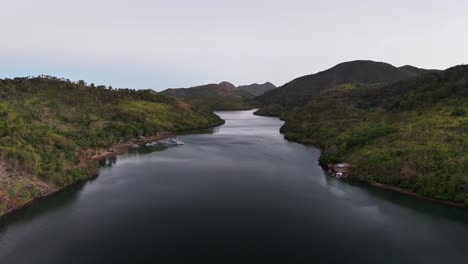 a serene bay nestled between green hills in sitio coring, western culion island, philippines, with calm waters and surrounding tropical vegetation creating a peaceful and remote natural setting