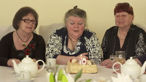 senior woman blowing out candles on birthday cake at dinner table