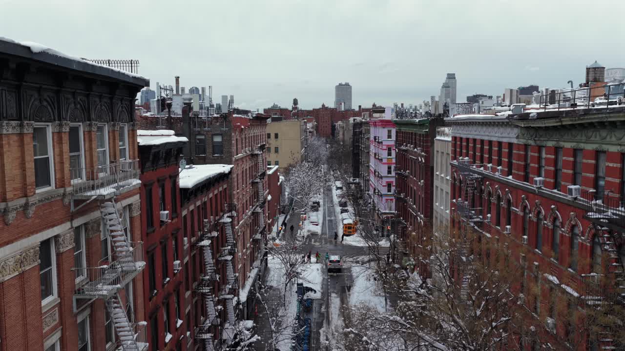 Sneklædt gade i New York City med historiske lejlighedsbygninger i mursten og brandtrapper samt vinter-skyline i baggrunden. Bydel i udkanten af Downtown på en kold vinterdag. Stigende vidvinkeloptagelse fra luften.