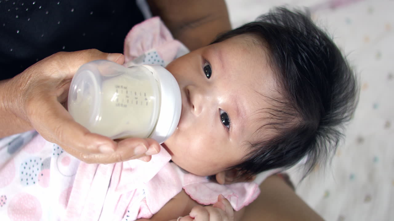 Baby girl receiving milk from a bottle, tenderly fed by her mother. A touching moment of care, promoting healthy growth, bonding, and the essentials of infant nutrition.