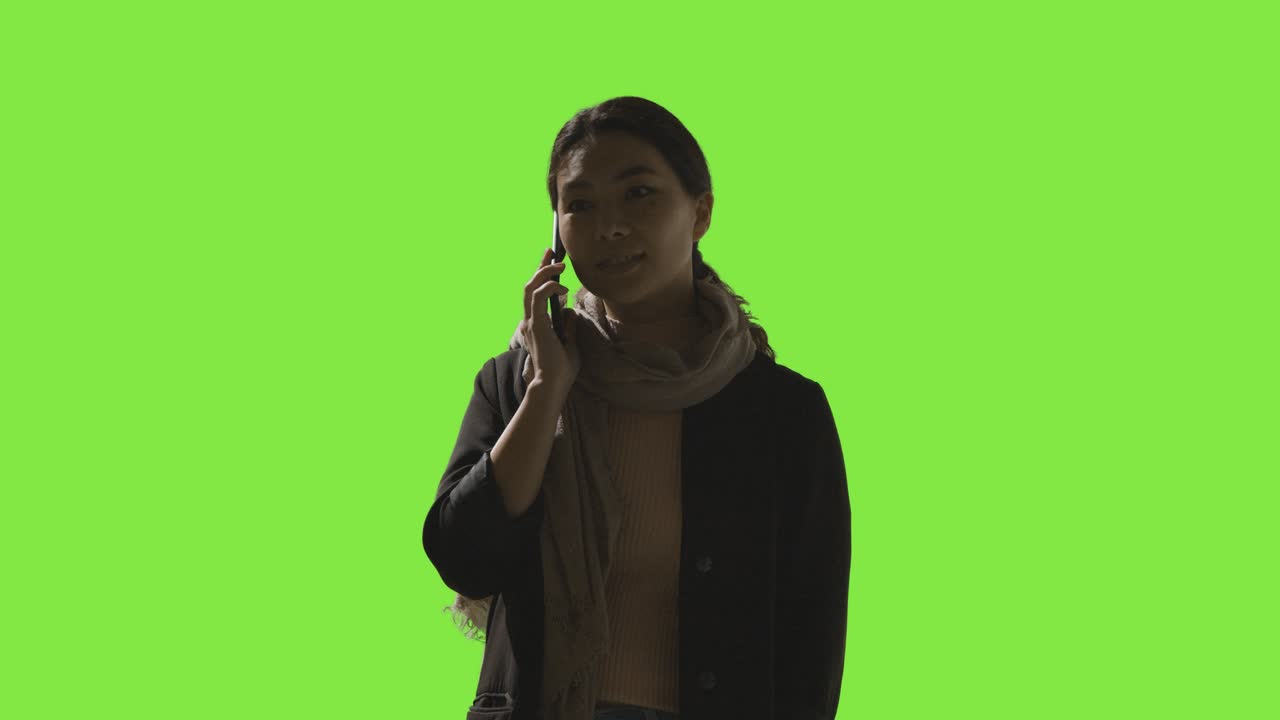 Ripresa in studio a bassa chiave di donna che risponde a una chiamata sul cellulare su sfondo verde