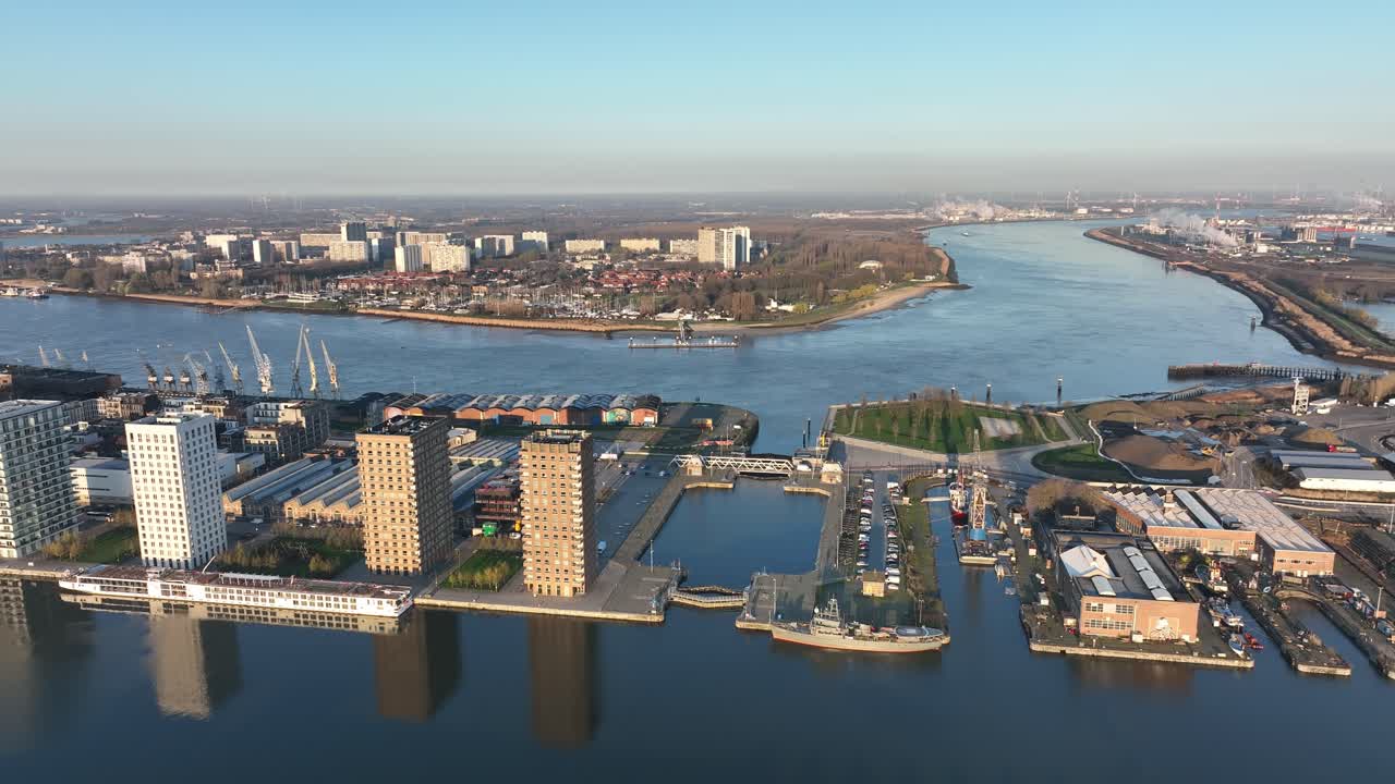 Pan left aerial shot of Antwerp river with harbor docks, residential buildings and surrounding urban landscape on a clear sunny day