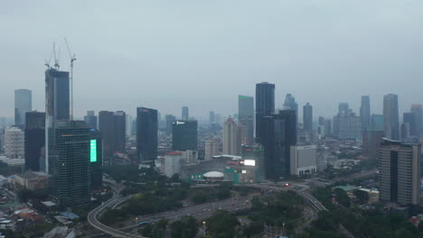 Toma-Aérea-De-Carro-Volando-Sobre-La-Intersección-De-La-Autopista-De-Varios-Carriles-Hacia-Los-Rascacielos-En-El-Centro-Urbano-De-Yakarta-Al-Atardecer