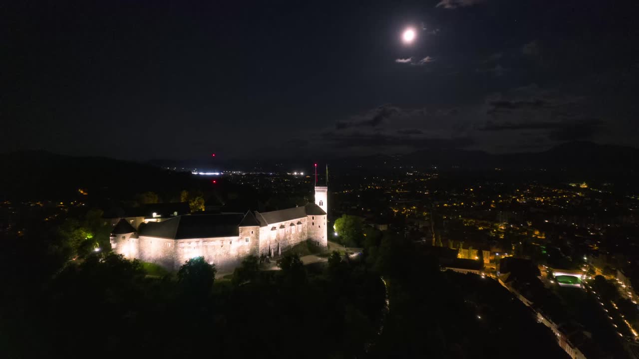 hiperlapso aéreo nocturno del castillo de ljubljana, volando bajo la luz de la luna llena, luces de la ciudad drone