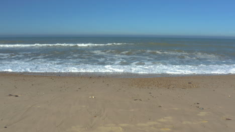 stable shot slowly pulling back from the waves crashing on a empty, golden beach