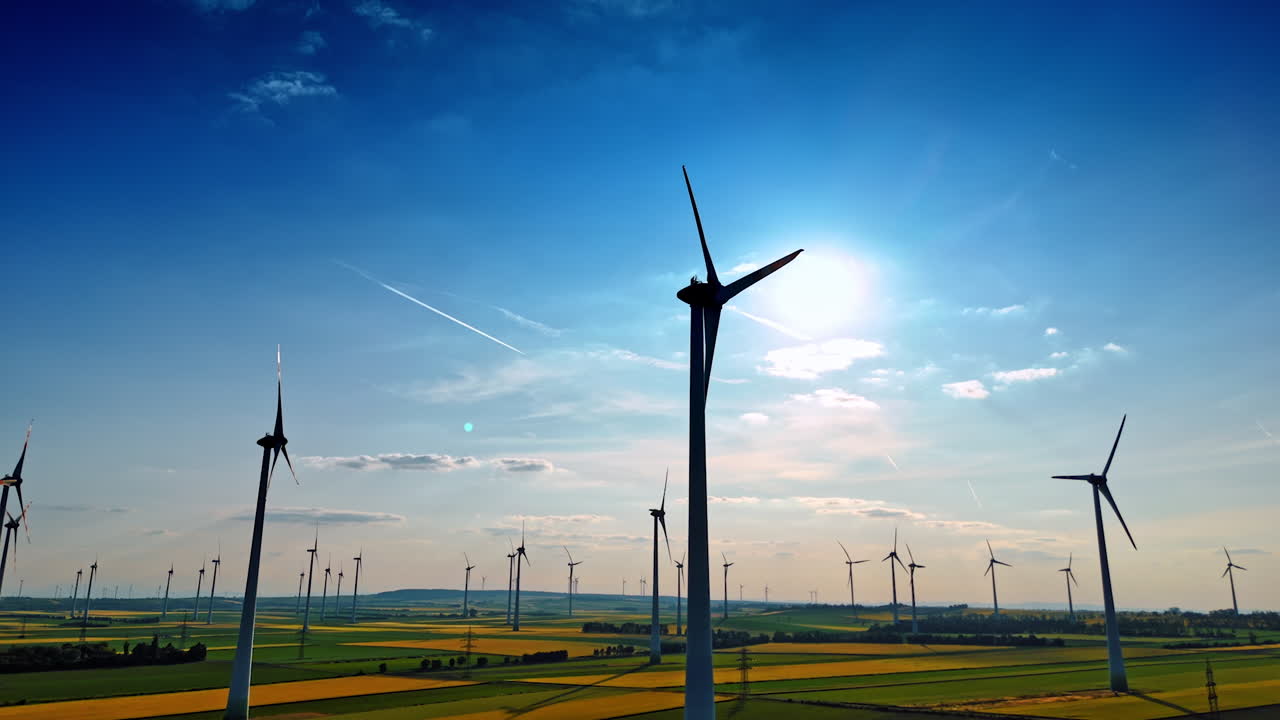 Turbines under blue clouds. Numerous wind turbines stand tall in a lush green landscape under a bright blue sky with scattered clouds
