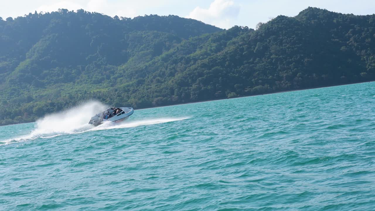 A speedboat races across turquoise waters near Phuket, Thailand, with lush green hills in the background under bright daylight