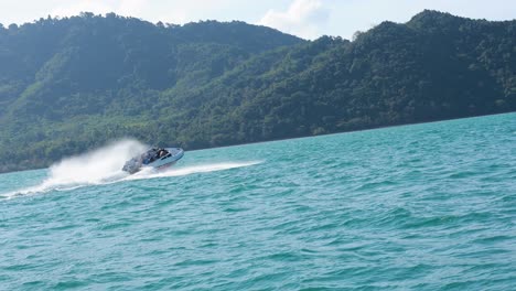 a speedboat races across turquoise waters near phuket, thailand, with lush green hills in the background under bright daylight