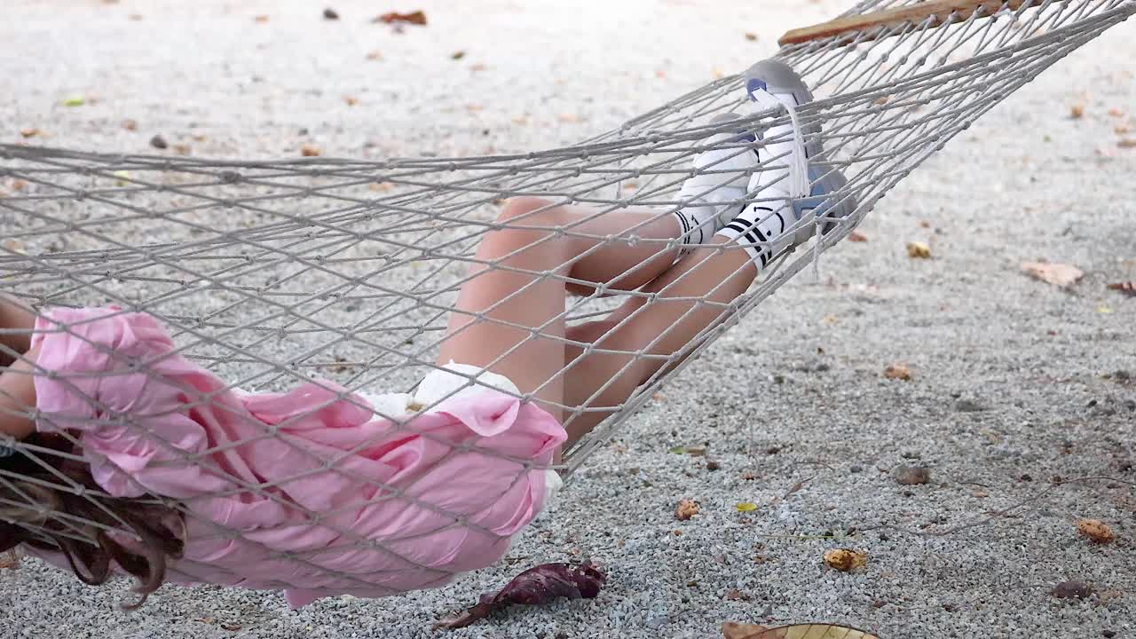 A woman in a pink dress relaxes on a hammock, gently swaying in a serene outdoor setting in Phuket