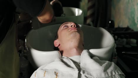 Close-up-view-of-hairdresser-hands-washing-male-head-at-barber-shot.-Hairdresser-washing-attractive-man's-hair