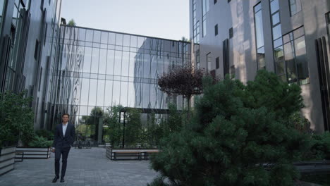 hombre de negocios confiado caminando edificio de oficinas. jardín ajardinado en el centro de la ciudad