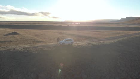 Rising-Aerial-Shot-of-a-Couple-Stood-by-their-Car-on-a-Road-Trip