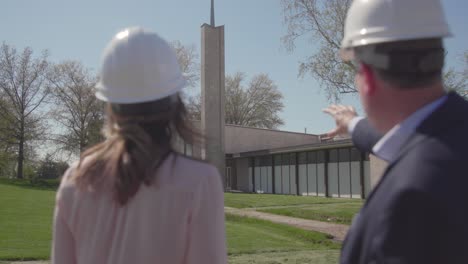 back shot of two architects in white construction helmets discussing outside in a sunny day