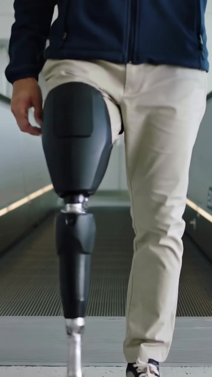 Vertical video: Walking man in coat nearing belt end, stepping to floor using left prosthesis