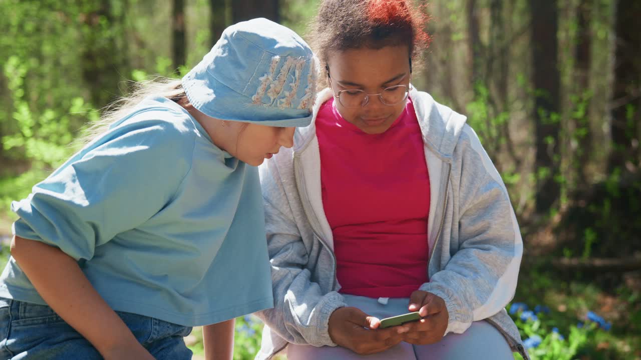 Two Girls Sharing a Smartphone in a Forest