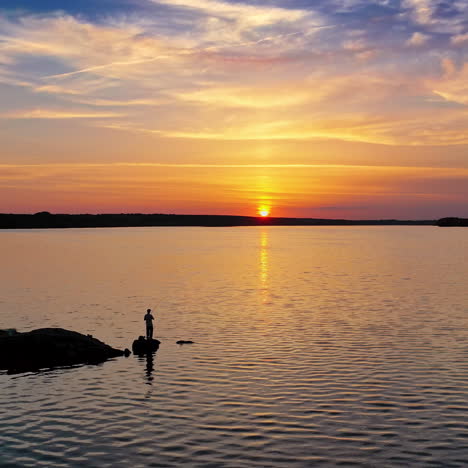 silhouette of a fisherman with fishing rod standing on stone near the river at sunset. evening background over the water and people having great time at the river. aerial view.