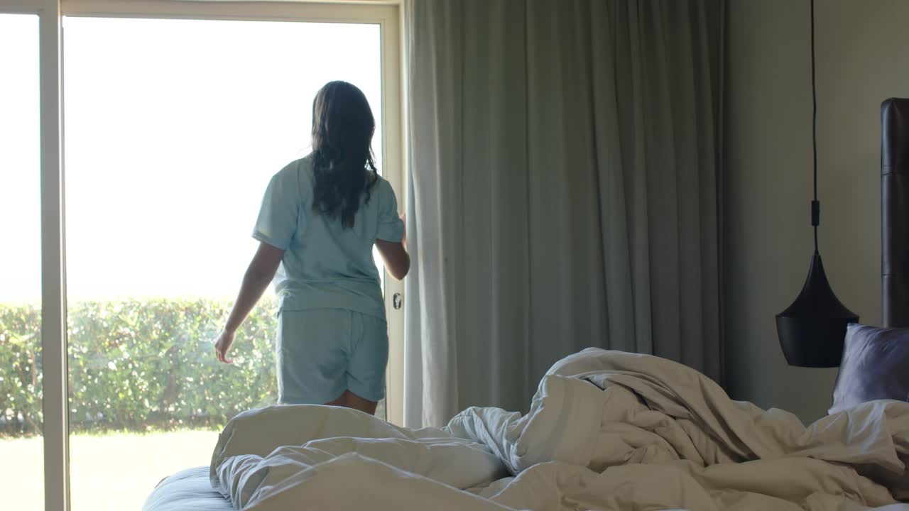 Người phụ nữ thức dậy, đứng dậy khỏi giường trong phòng ngủ, kéo rèm cửa, mở cửa trượt, nhìn ra bên ngoài.