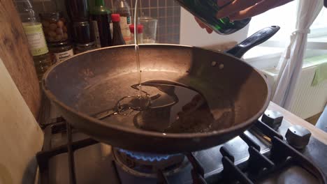 domestic chef pouring olive oil into hot frying pan on kitchen gas hob