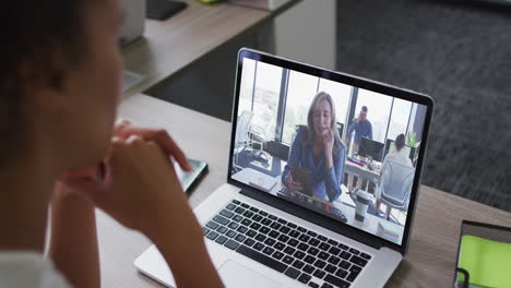 african american businesswoman sitting at desk using laptop having video call with female colleague