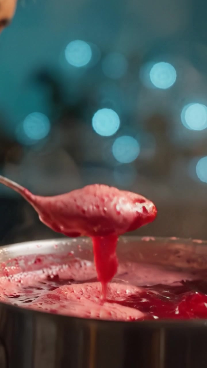 Una vista ravvicinata di salsa di frutti di bosco fatta in casa mentre viene mescolata, che mostra consistenza e colore in una delizia culinaria con luci bokeh sullo sfondo.
