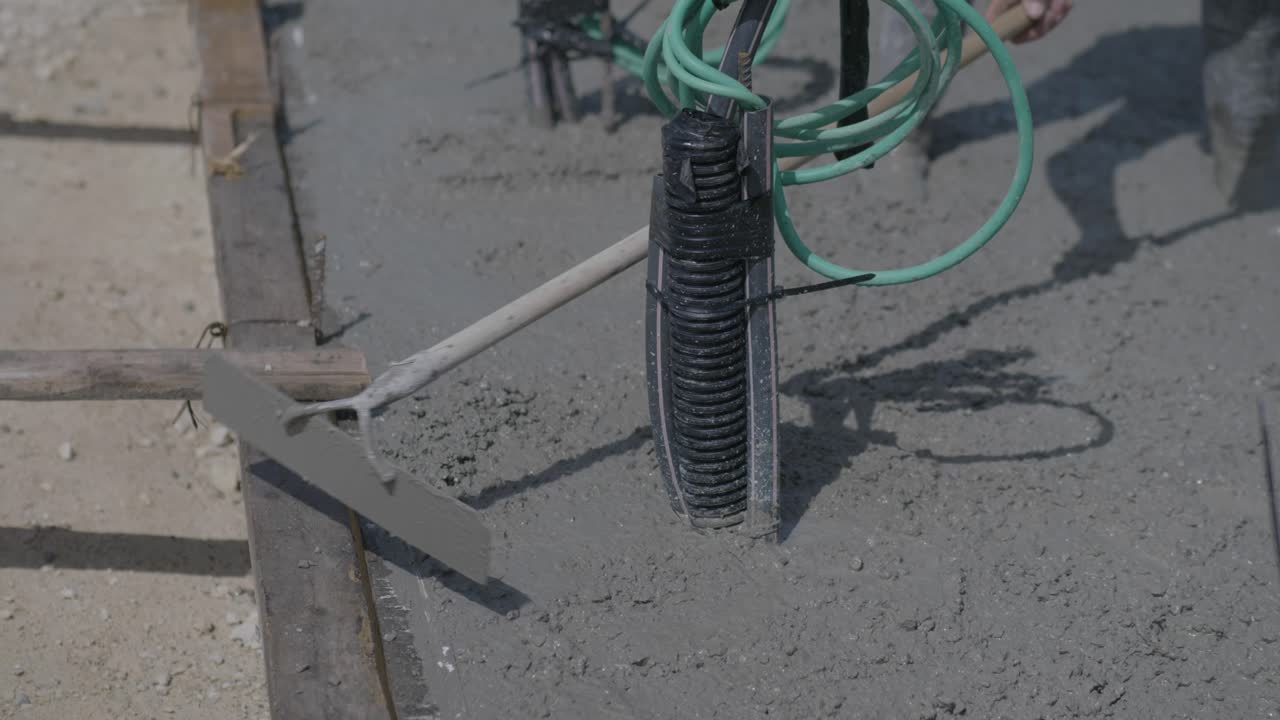 Close-up of electrical conduit and green wires embedded in wet cement during construction.